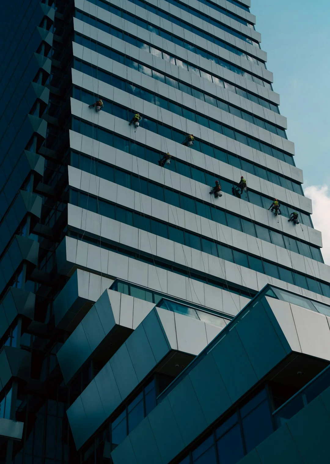 Two workers cleaning windows on a glass building facade using a lift platform, enhancing building aesthetics.